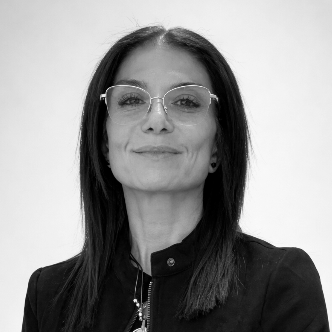 Black-and-white professional headshot of Mitra Shaffy, Marketing Director in Florida, wearing glasses and a dark jacket, facing forward with a confident, approachable expression against a clean background.